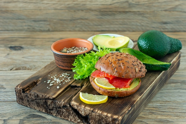 Hamburger di salmone biologico fatto in casa con pomodoro, insalata di mais e avogado su un piatto su sfondo di legno. Cibo biologico sano.