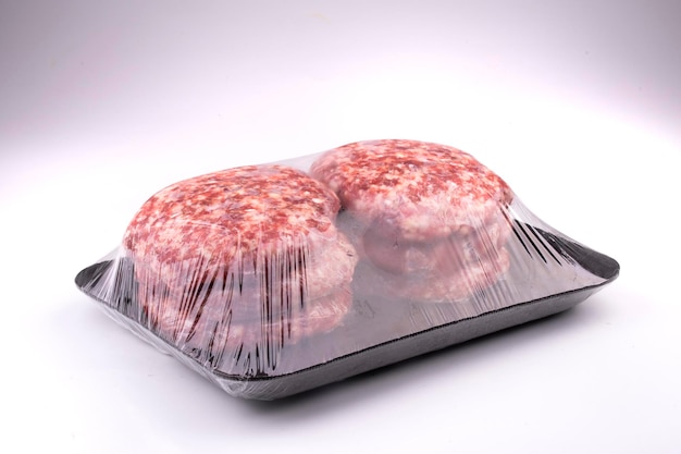 Hamburger fatti a mano crudi confezionati con carta per pellicola in vassoio di polistirolo nero isolato su sfondo bianco