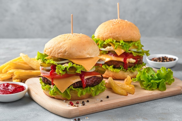Hamburger fatti in casa con manzo, formaggio e verdure su un muro grigio. Vista laterale, orizzontale.