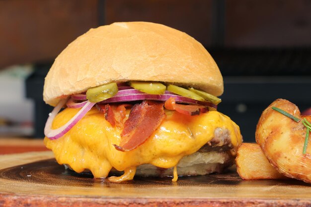 Hamburger fatto alla griglia del barbecue con formaggio, bacon, cipolla, sottaceto su fondo in legno