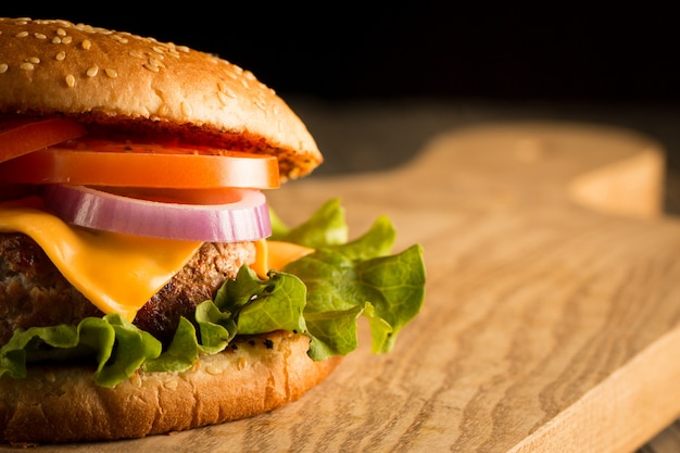 Hamburger fatto in casa con carne di manzo, cipolla, pomodoro, lattuga e formaggio. Fine fresca dell'hamburger su sulla tavola rustica di legno con le patate fritte, la birra e le patatine fritte. Cheeseburger.