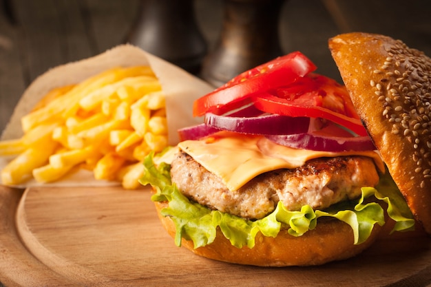 Hamburger fatto in casa con carne di manzo, cipolla, pomodoro, lattuga e formaggio. Fine fresca dell'hamburger su sulla tavola rustica di legno con le patate fritte, la birra e le patatine fritte. Cheeseburger.