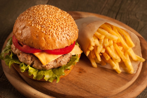 Hamburger fatto in casa con carne di manzo, cipolla, pomodoro, lattuga e formaggio. Fine fresca dell'hamburger su sulla tavola rustica di legno con le patate fritte, la birra e le patatine fritte. Cheeseburger.