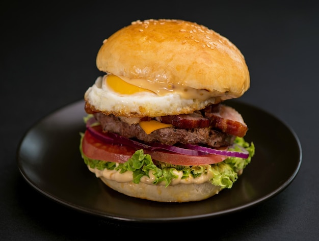 Hamburger grande e gustoso con uovo di lattuga di cotoletta di manzo e formaggio su sfondo nero