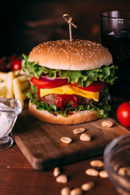 Hamburger gustoso fresco fatto in casa con lattuga e formaggio sulla tavola rustica in legno. Patatine fritte, pomodori e salsa. Sfondo di cibo scuro.