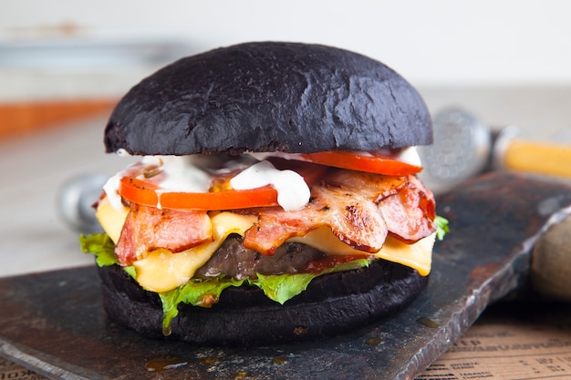 Hamburger nero con carne su tavola rotonda in legno con ascia