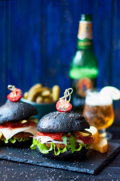 Hamburger nero con manzo, insalata e patatine fritte. Birra fresca in un bicchiere. Tendenze del cibo di strada. Una cena calorica. Copia spazio