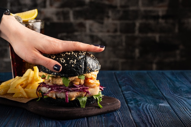 Hamburger nero con pesce e gamberi, Fishburger con gamberi, La mano femminile preme l'hamburger in cima