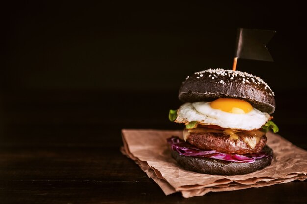 Hamburger nero delizioso e succoso con una grande cotoletta di carne su sfondo nero