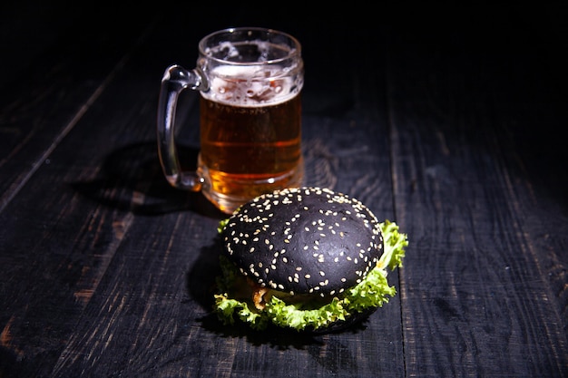 Hamburger nero e bicchiere di birra isolati sul nero. focalizzazione morbida. messa a fuoco selettiva.
