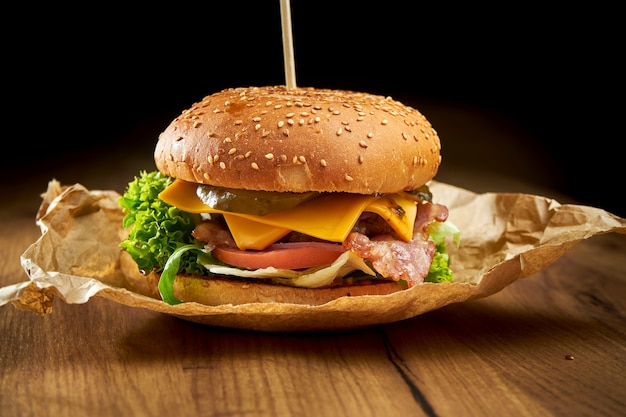 Hamburger succoso con carne di manzo, insalata, sottaceti, formaggio cheddar baconnd, servito su pergamena sul tavolo di legno