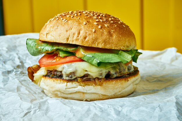 Hamburger succoso con formaggio fuso con un tortino di carne su carta artigianale. Tavolo giallo. Street, fast food ...