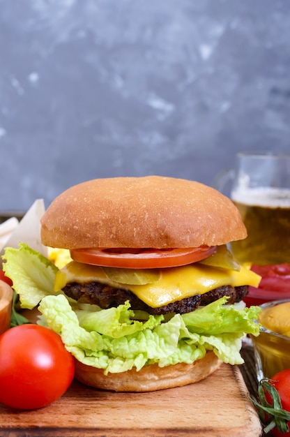 Hamburger succoso, patatine fritte, salse, birra su un fondo di legno.