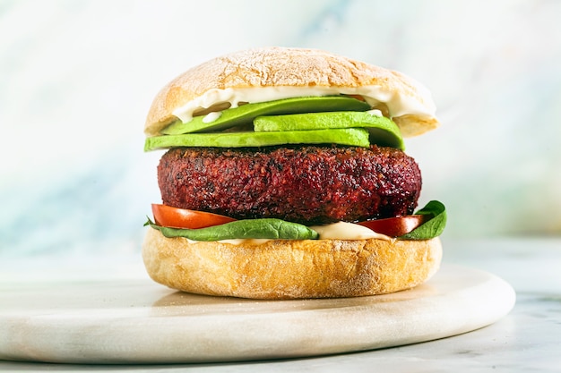 Hamburger vegano senza carne con avocado, pomodori e spinaci sul tavolo e vino rosso in un bicchiere