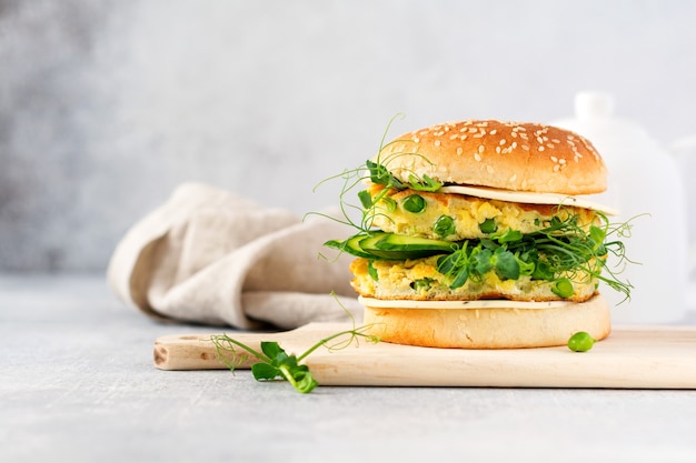 Hamburger vegetariano sano con uova e germogli di piselli e semi microgreen, insalata fresca, fetta di cetriolo su una tavola di legno da taglio su sfondo chiaro. Messa a fuoco selettiva