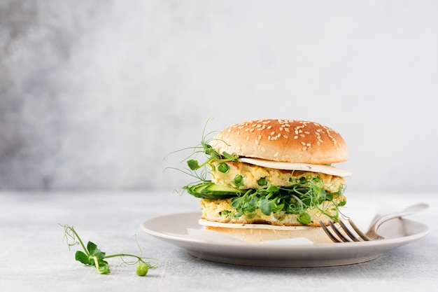 Hamburger vegetariano sano con uovo e piselli germogli e semi microgreen, insalata fresca, fetta di cetriolo su una tavola di legno di taglio su sfondo chiaro. Messa a fuoco selettiva.