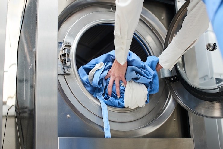 Hands loading laundry into washing machine in dry cleaning