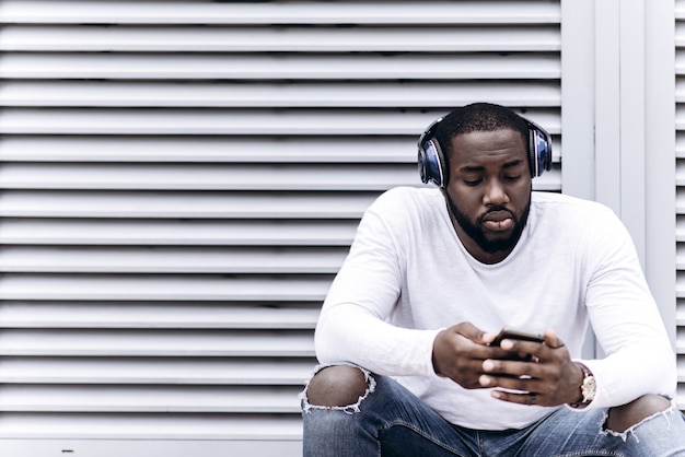 Handsome afro americano che indossa abiti casual nella città moderna ascoltando musica con le cuffie