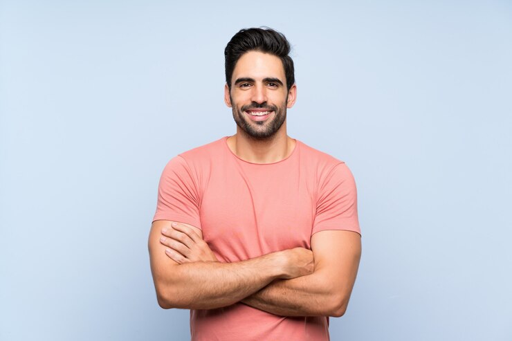 Photo handsome young man in pink shirt over isolated blue wall keeping the arms crossed in frontal position