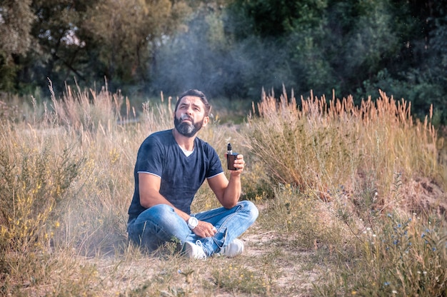 Handsomeman fuma vape espira il fumo all'aperto. La nuova sigaretta tecnologica.