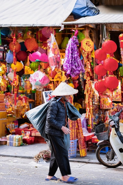 Hanoi, Vietnam - 21 febbraio 2016: La donna del venditore indossa il tradizionale cappello vietnamita nel mercato di strada nella città vecchia di Hanoi in Asia in Vietnam. Negozio che vende lanterne. Commercio di imprese locali