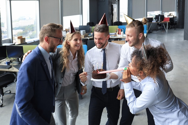 Happy business team con torta di compleanno saluta il collega alla festa in ufficio.