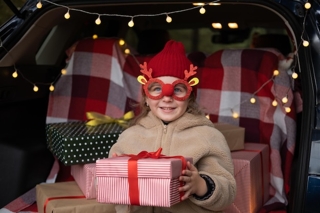 happy child girl having fun in decorated trunk of a car with Christmas gifts