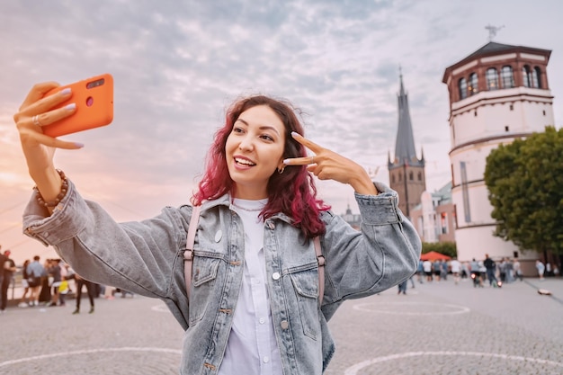 Happy girl travel blogger scatta foto selfie sul suo smartphone nella città vecchia di Dusseldorf sull'argine e la passeggiata del fiume Reno Viaggi e luoghi turistici tedeschi