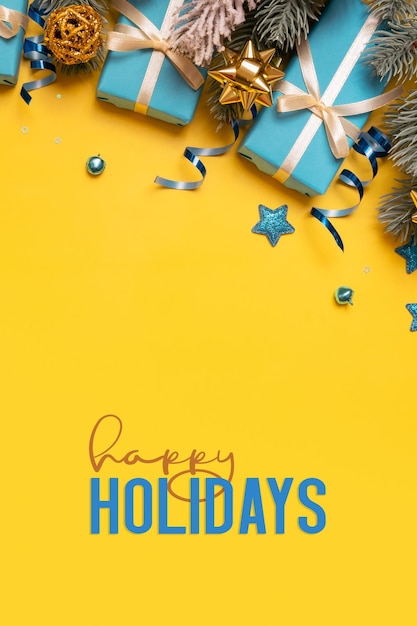 Happy Holidays testo su sfondo giallo con regali di pino blu e decorazioni festive vista dall'alto Biglietto d'auguri di Natale