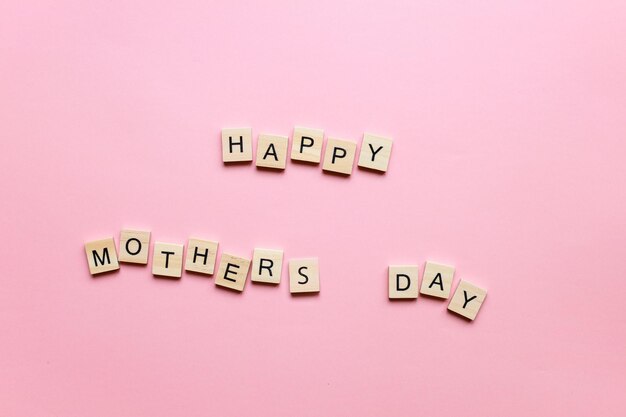 Happy Mothers Day fatto di lettere di legno su sfondo rosa Biglietto per la festa della mamma