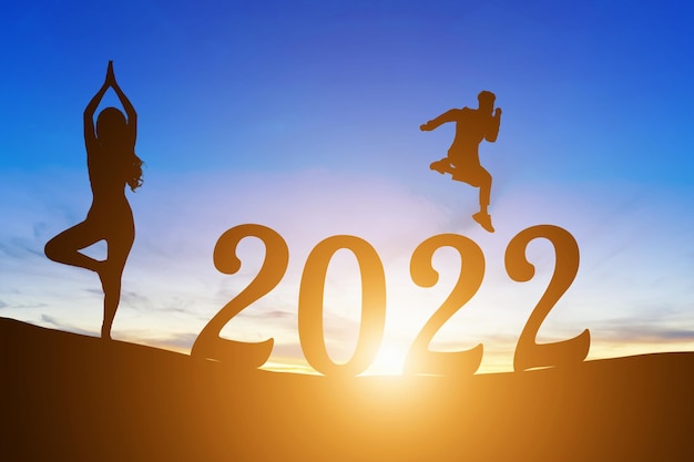 Happy New Year Numbers 2022, Silhouette un uomo bello che salta si sente felice di muoversi e donna che pratica yoga alba mattutina sullo sfondo dell'orizzonte, concetto di salute e felice anno nuovo.