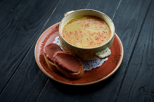 Harira marocchina, zuppa di lenticchie con coriandolo in un piatto rosso su uno sfondo di legno nero.