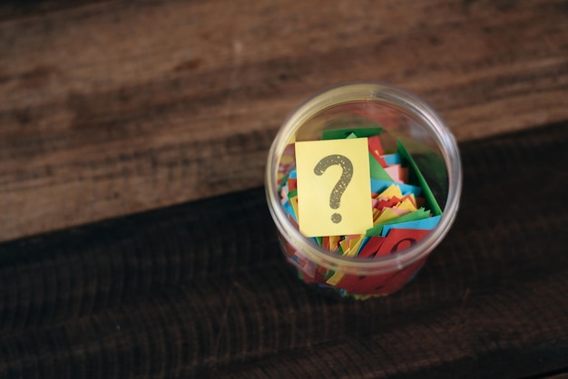 High angle view of question mark on yellow adhesive note in jar at table