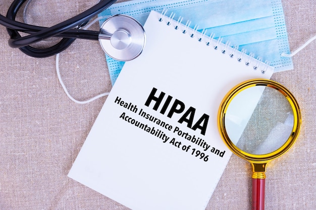 HIPAA, Health Insurance Portability and Accountability Act del 1996, testo scritto su blocco note bianco, maschera medica, stetoscopio, lente d'ingrandimento su sfondo di lino.