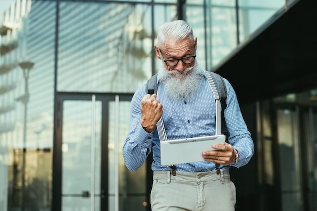 Hipster anziano con un tablet digitale contro l'edificio