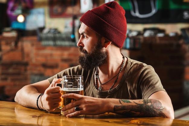 Hipster che si rilassa al bar con la birra Il bar è un luogo rilassante per bere e rilassarsi Uomo con la barba che beve birra