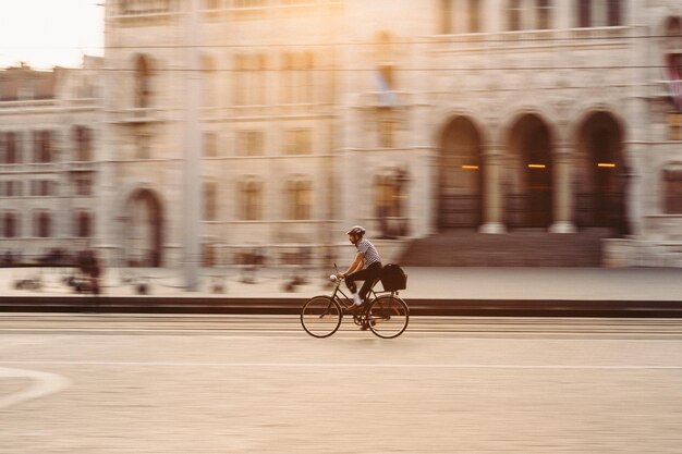 Hipster in sella a una bicicletta davanti al palazzo del parlamento di Budapest durante il tramonto primaverile