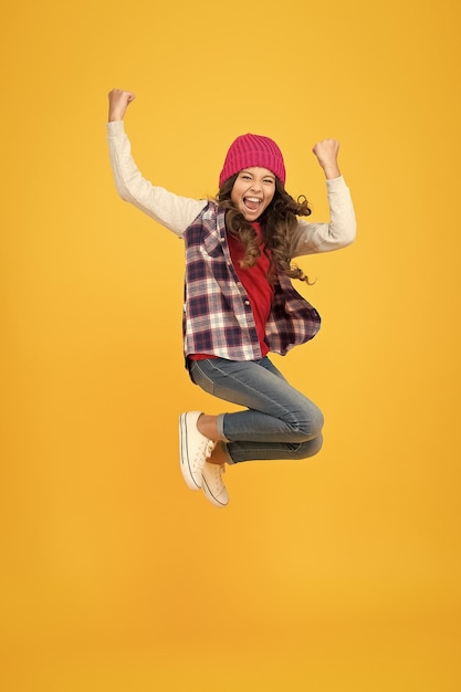 Hipster look allegro bambino in cappello lavorato a maglia denim moda stile scuola ragazza su sfondo giallo pieno di energia bambino moda e bellezza adolescente che salta in abiti casual stile infanzia felice