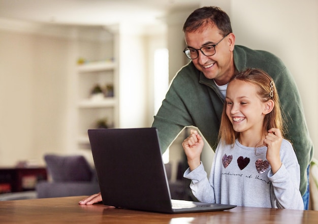 Ho superato gli esami a casa. Inquadratura di un'adorabile bambina seduta e che usa un laptop a casa mentre suo padre l'aiuta