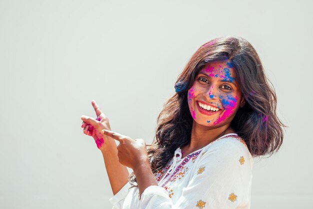 Holi Festival Of Colors Ritratto di felice ragazza indiana in holi color che punta le dita sullo sfondo bianco dello studio copyspase