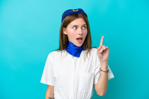 Hostess dell'aeroplano donna inglese isolata su sfondo blu pensando a un'idea che punta il dito verso l'alto