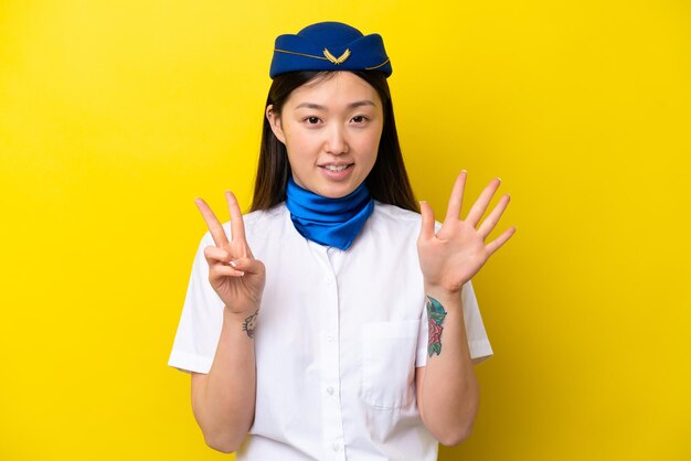 Hostess donna cinese dell'aeroplano isolata su sfondo giallo che conta sette con le dita