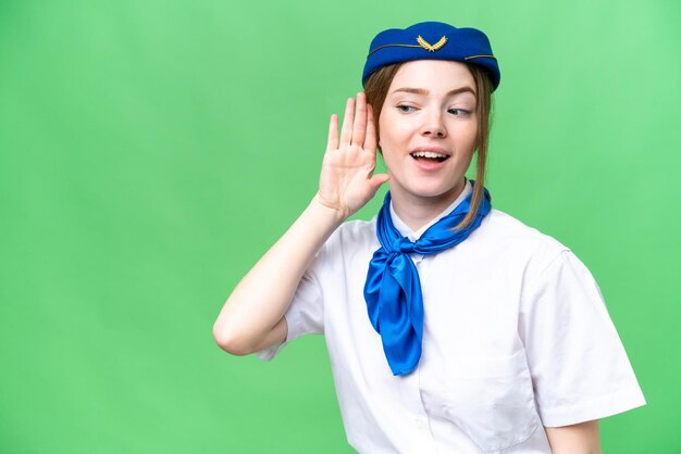 Hostess in aereo su sfondo chroma key isolato ascoltando qualcosa mettendo la mano sull'orecchio