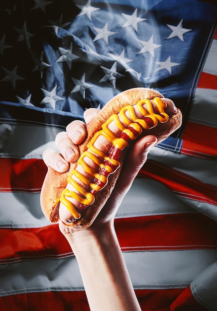 Hot dog americano classico in mano sullo sfondo della bandiera americana