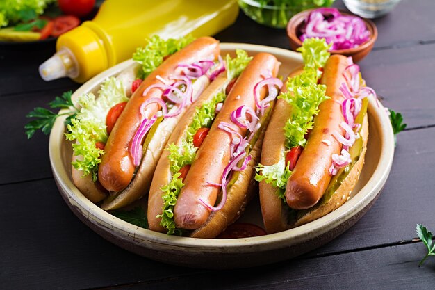 Hot dog con salsiccia in salamoia cetriolo pomodori cipolle rosse e lattuga su sfondo di legno scuro Hot dog estivo