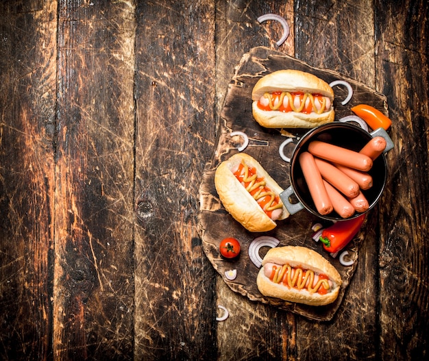 Hot dog con senape, cipolle e pomodori sulla tavola di legno.