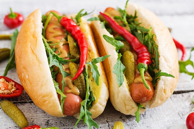 Hot dog con sottaceti, capperi e rucola su sfondo di legno.