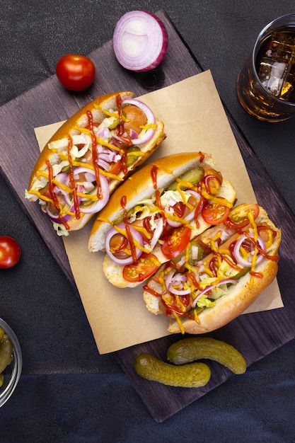 Hot dog con verdure, senape e ketchup su un tagliere su uno sfondo scuro, vista dall'alto