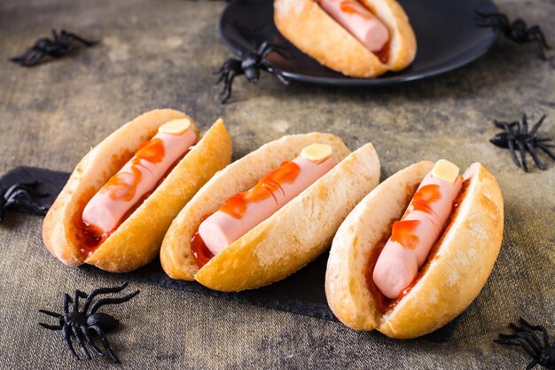 Hot dog di salsiccia e formaggio in ketchup in panini su ardesia ricetta di Halloween