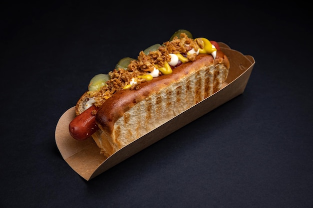Hot dog in piatti di carta con salsicce e salsa su sfondo nero